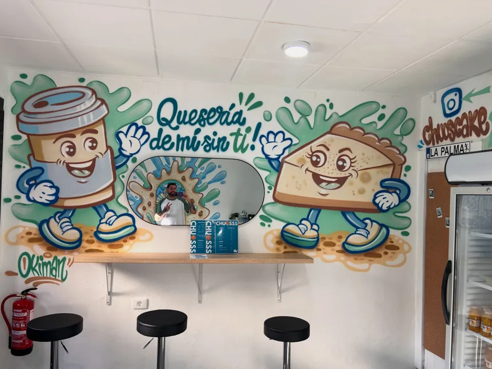 Mural en una cafetería con un vaso de café y un trozo de tarta con cara, y la frase «Qué sería de mí sin ti»