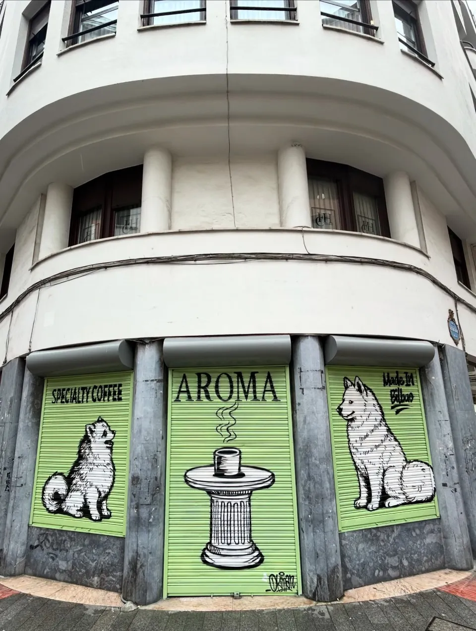 Tres persianas verdes de una cafetería con dos perros y una taza de café humeante