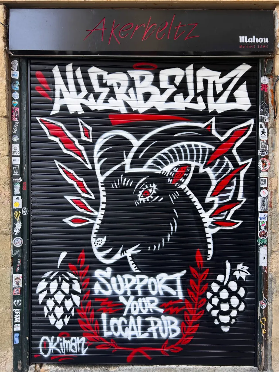 Persiana negra de un pub con una cabra blanca y roja y el lema «Support your local pub»